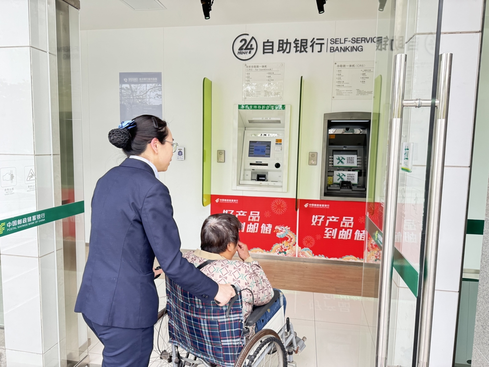 邮储银行工作人员帮忙老人推轮椅(1)